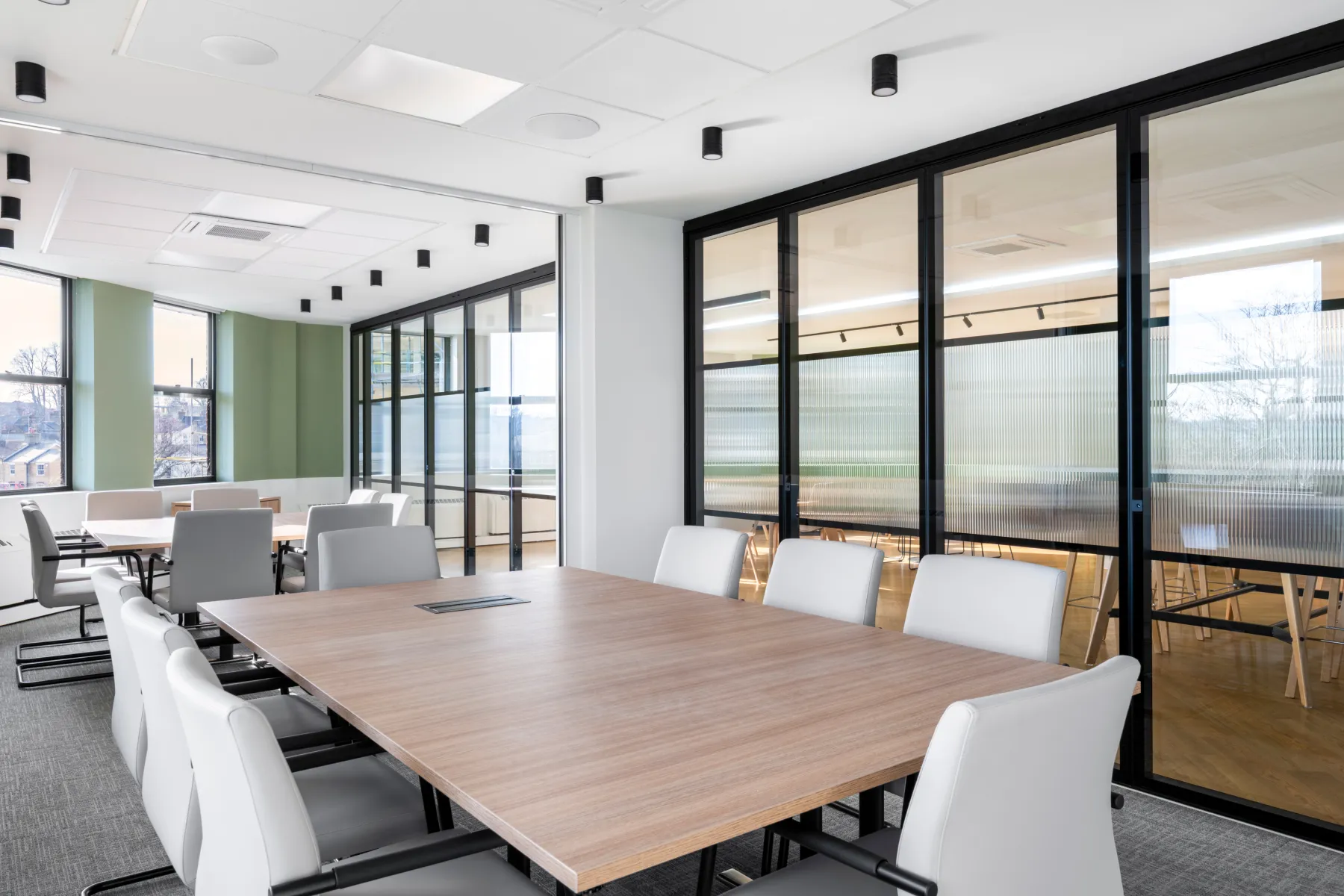 Modern joint meeting room, a larger board table in wood and a smaller one. The room has glass windows with black frames.