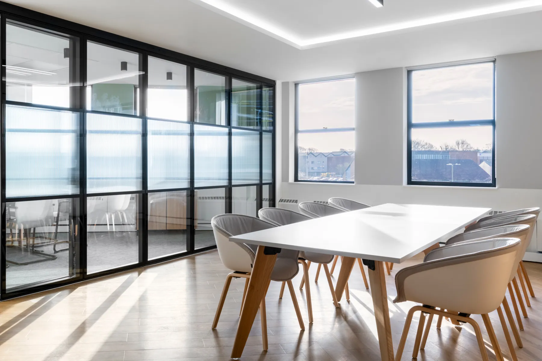 A modern table with bucket style seats in white. Glass panels framed in black in the background