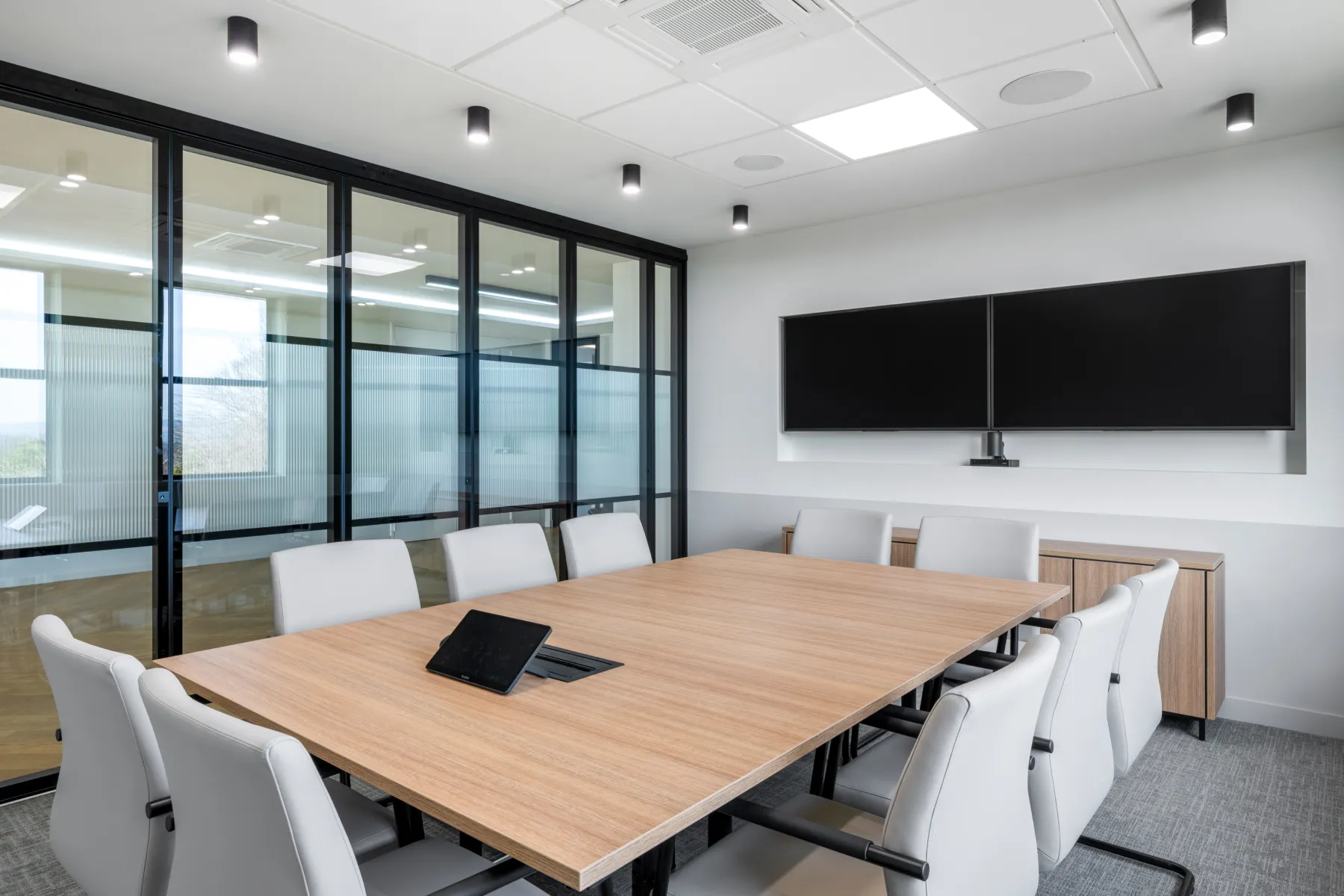 A board room with the same windows and black frames. Large wooden board table, white chairs and screens on the wall.