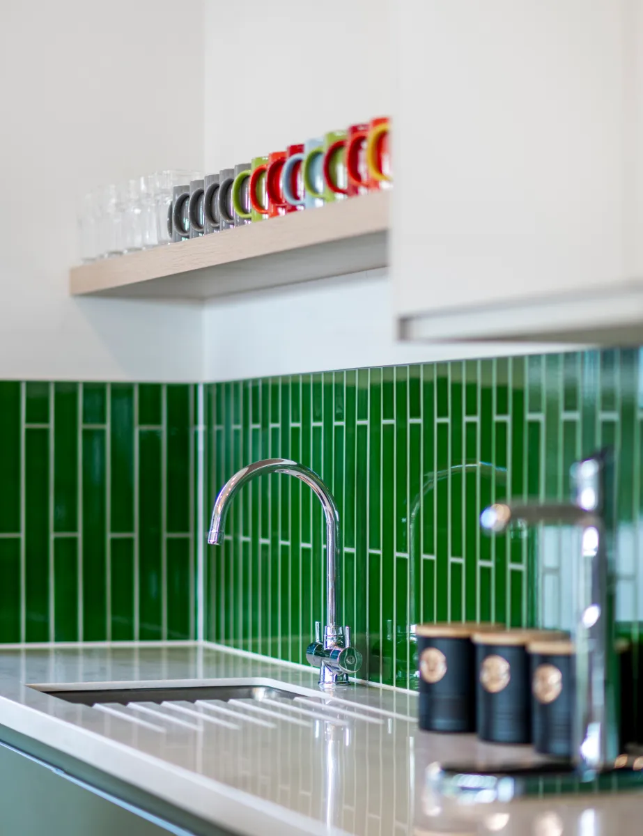 A lovely kitchenette, with retro green tiles and white cupboards. 