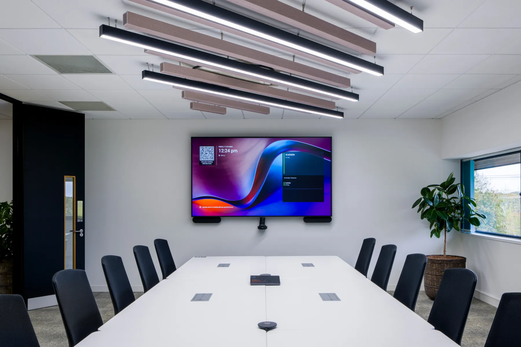 Large boardroom with a central white table, integrated AV technology, ceiling baffles, and natural light from expansive windows.