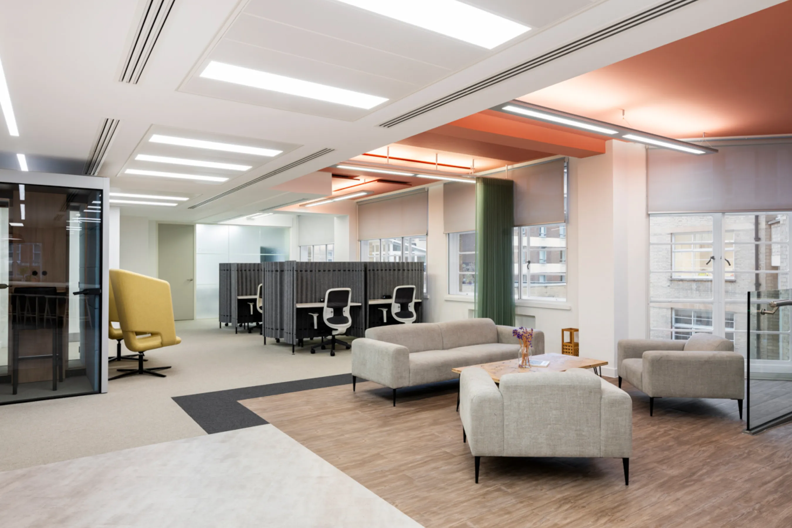 Open-plan office lounge with sofas, desks, and warm ceiling lighting.