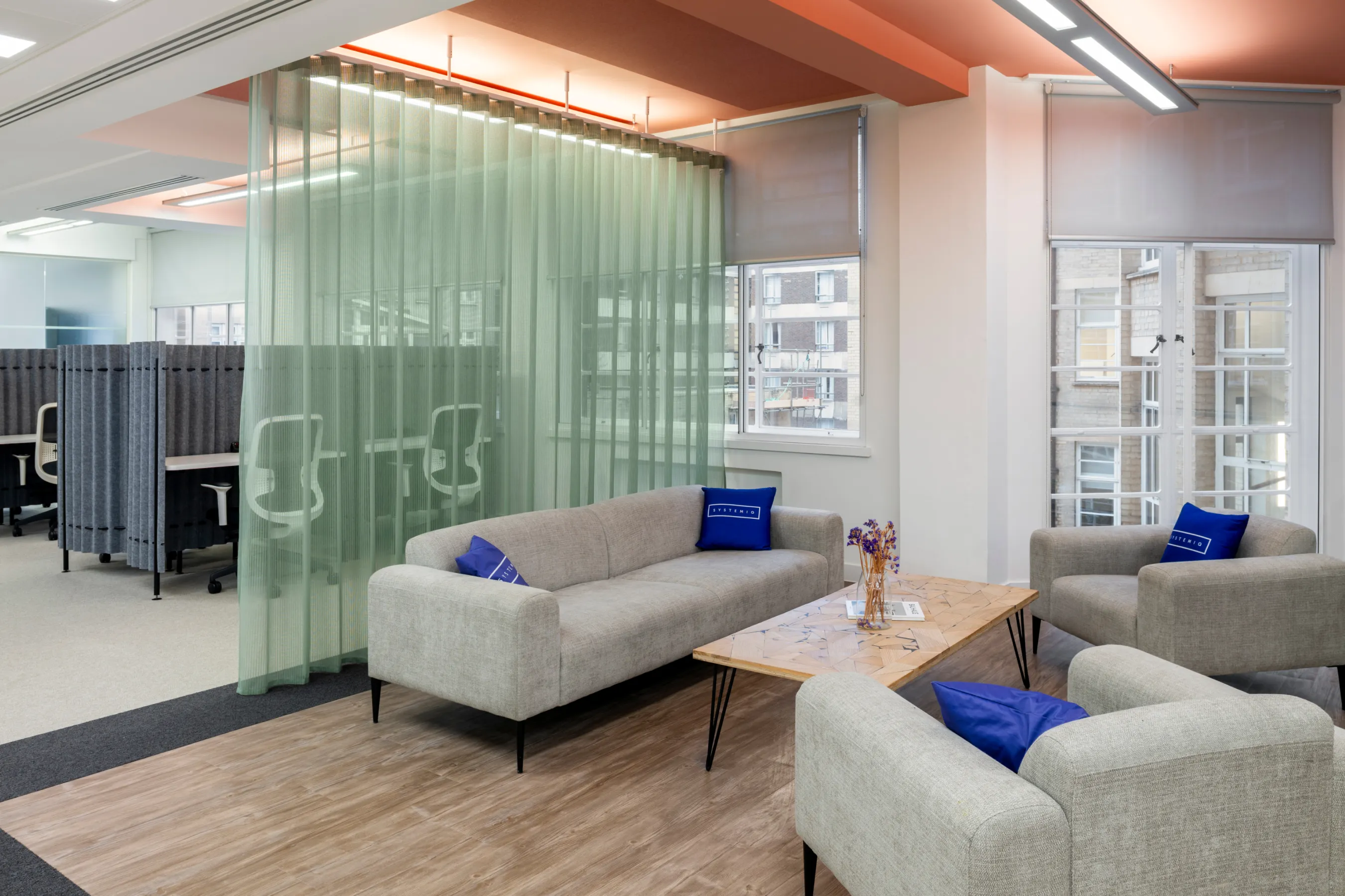 Modern office lounge with white sofas, glass partitions, and warm lighting.