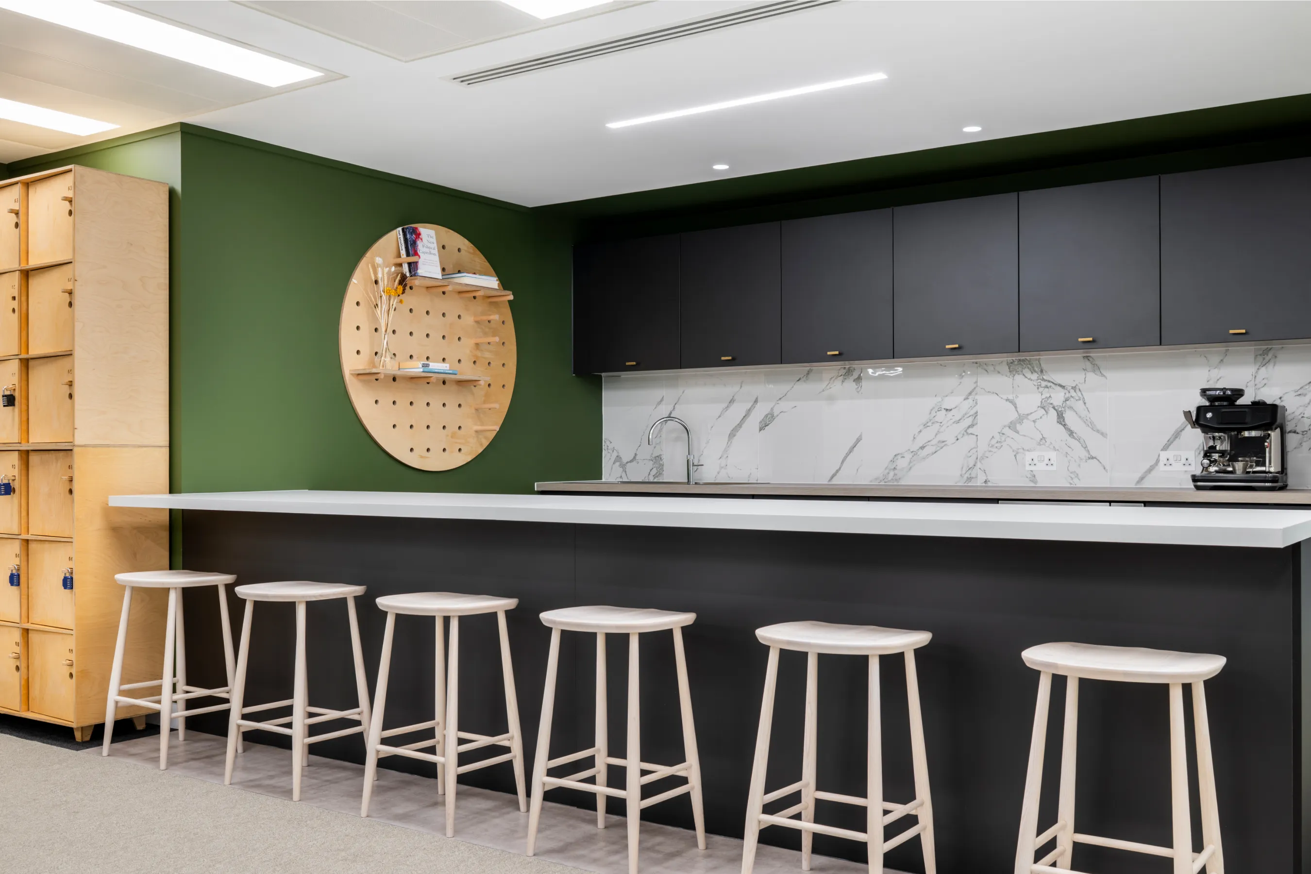 Office kitchenette and bar area with stools, wood panelling, and dark feature wall.