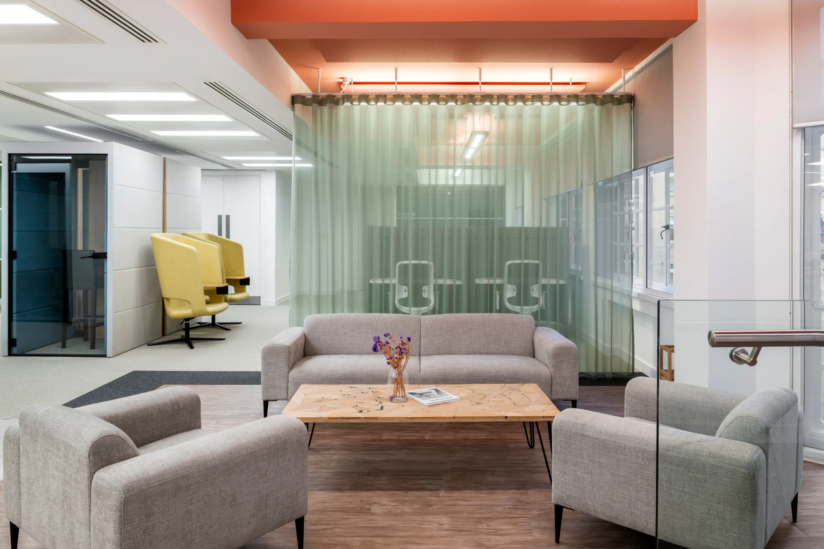 Lounge area with sofas, glass partitions, and soft lighting in a modern office.