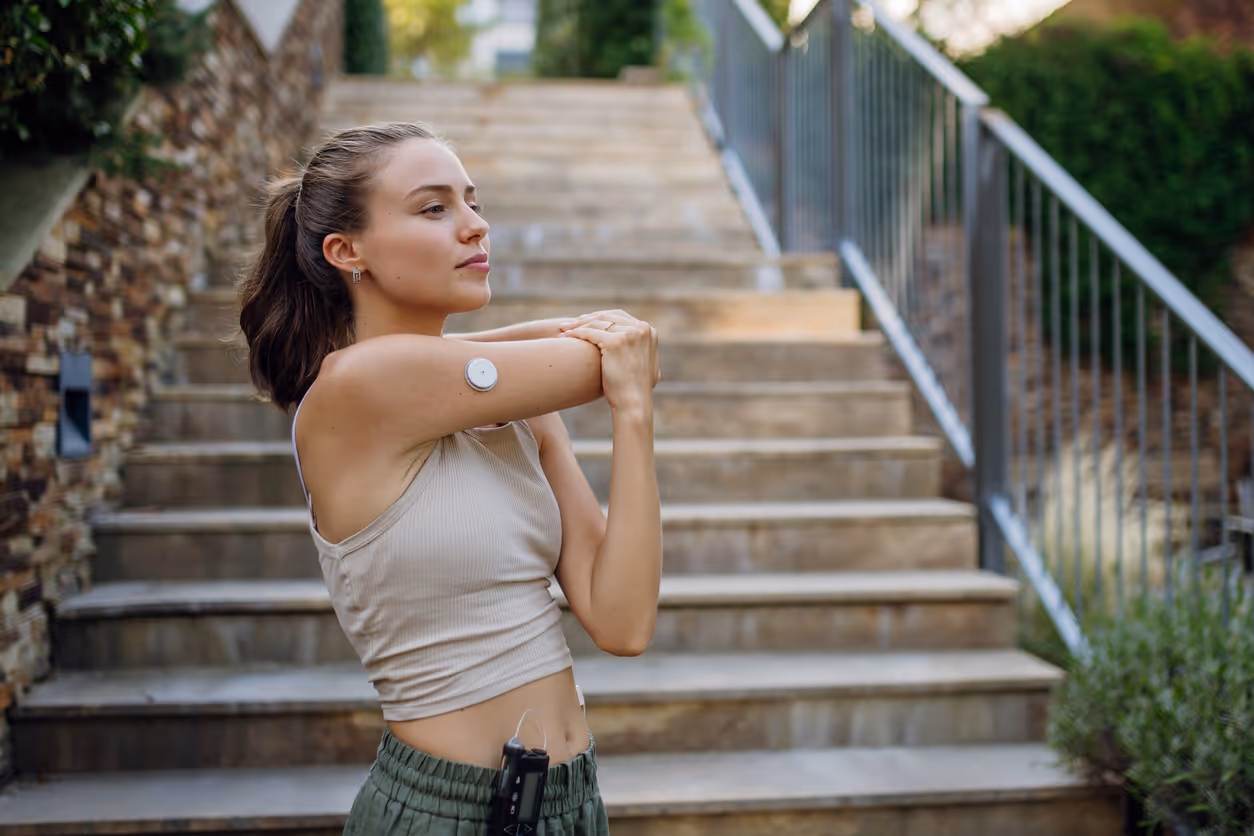 Frau mit Sensor auf dem Oberarm macht Dehnübungen vor einer Steintreppe im Freien.