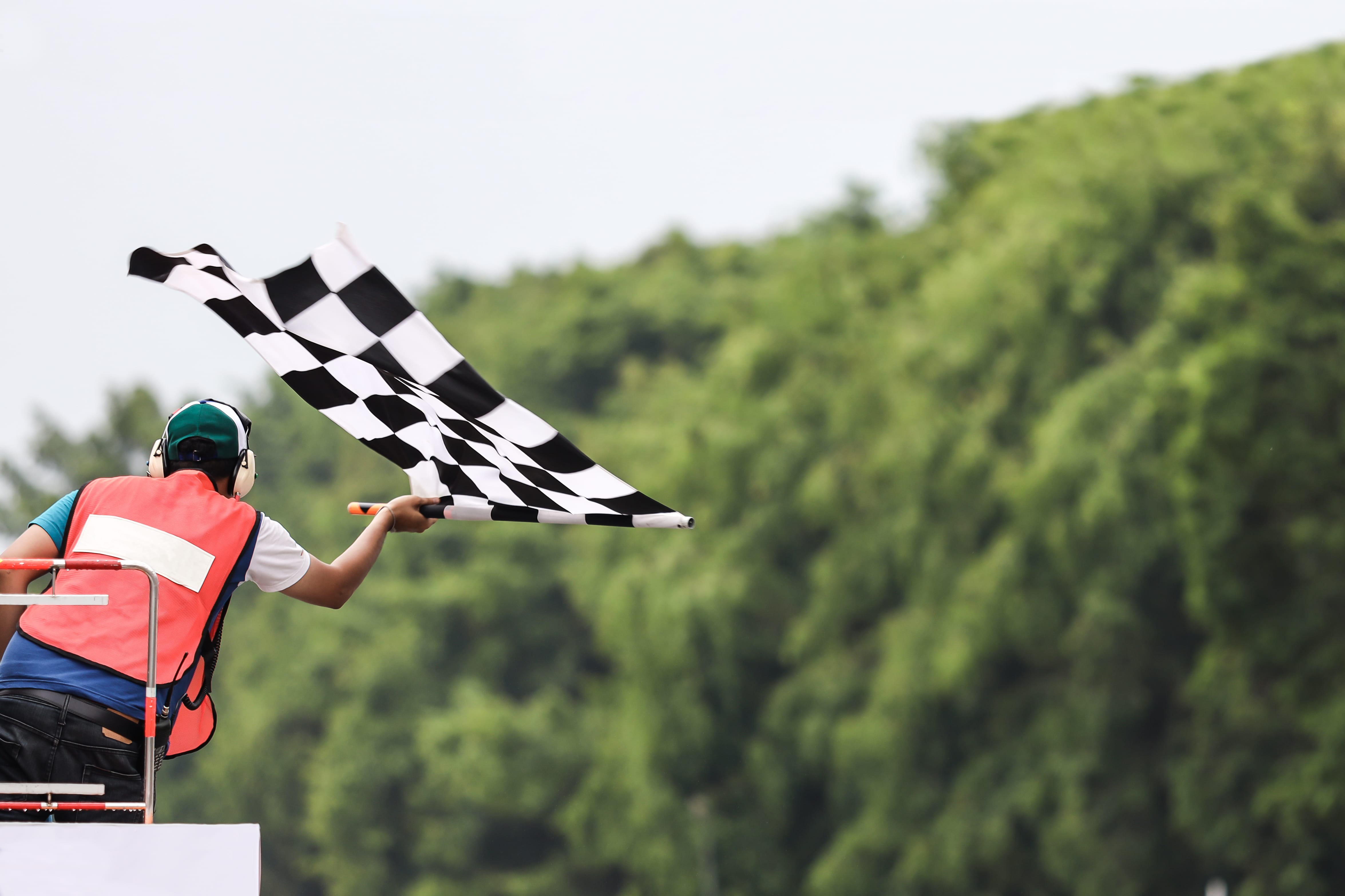 Photo of the finish of a car race, the race director is photographed from behind waving the finish flag