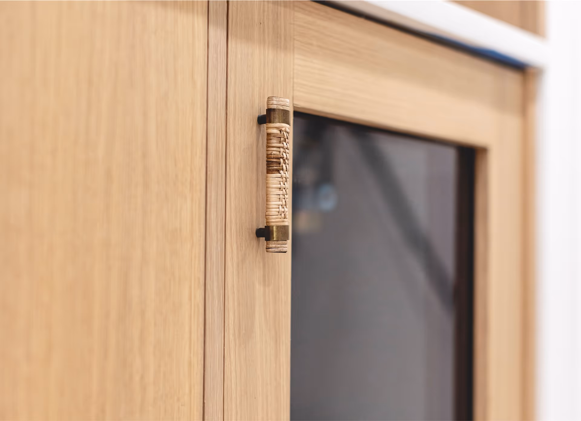 Close-up of a modern wooden cabinet door with a woven rattan handle and a glass panel.
