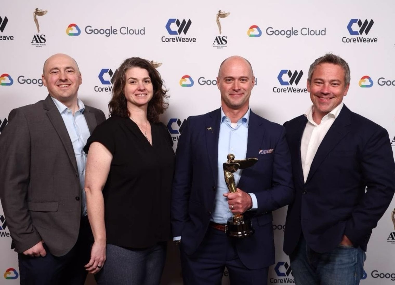 Four professionals posing at an awards event, with one person holding a trophy, standing in front of a backdrop featuring CoreWeave, Google Cloud, and AIS logos.