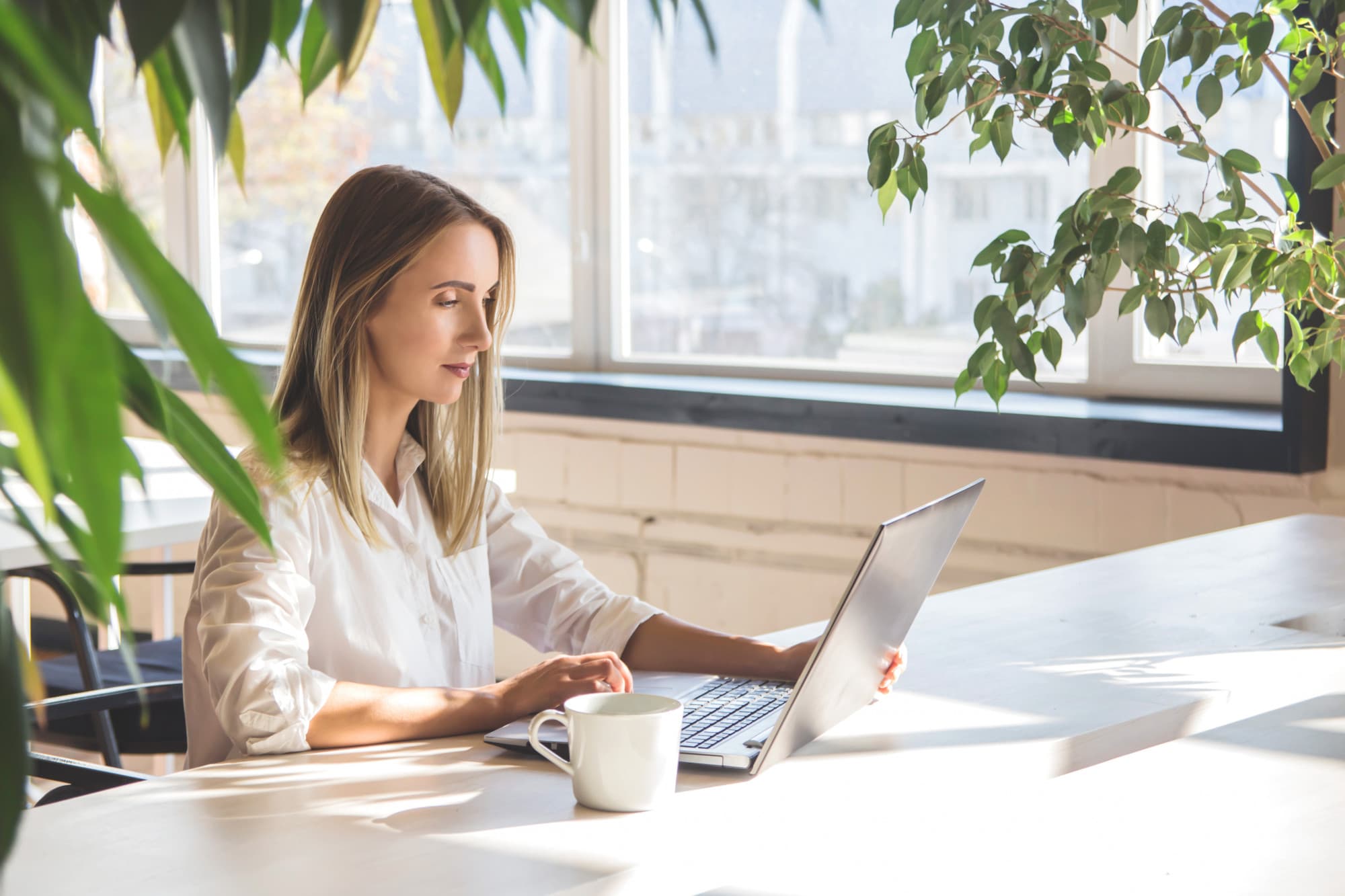 Smiling woman with long hair and wireless earbuds sitting on a wooden bench outdoors using a laptop.
