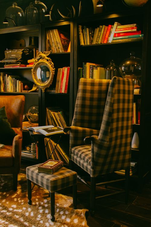 plaid handmade chair in front of bookshelf adorned with books and knick knacks in the cozy library room at The Federal Inn in Maumee Ohio