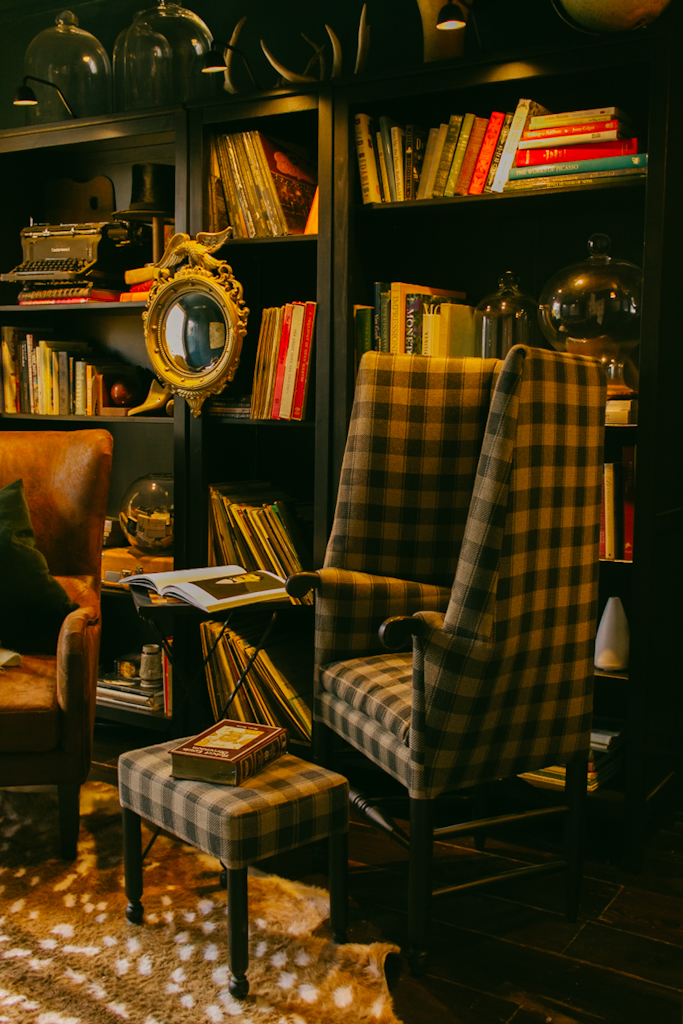 plaid handmade chair in front of bookshelf adorned with books and knick knacks in the cozy library room at The Federal Inn in Maumee Ohio