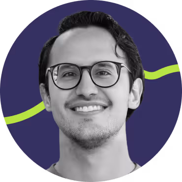 Smiling man with dark hair and glasses in front of a purple background with a green wavy line.