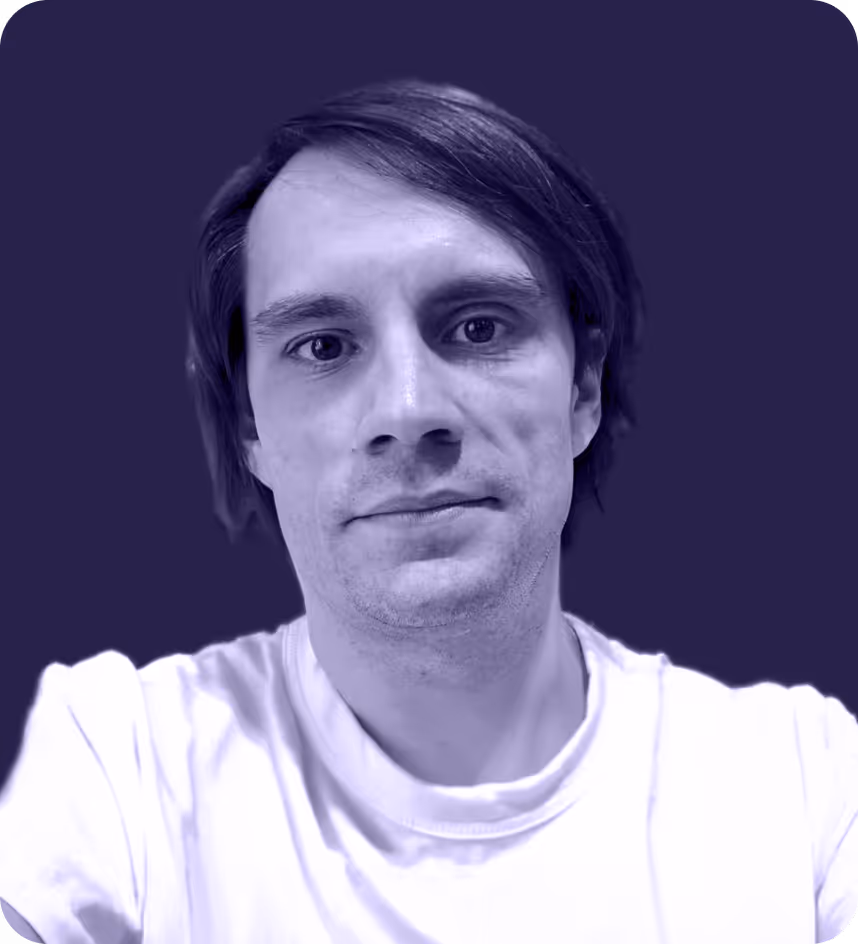 Close-up of a young man with short dark hair wearing a white shirt against a dark purple background.