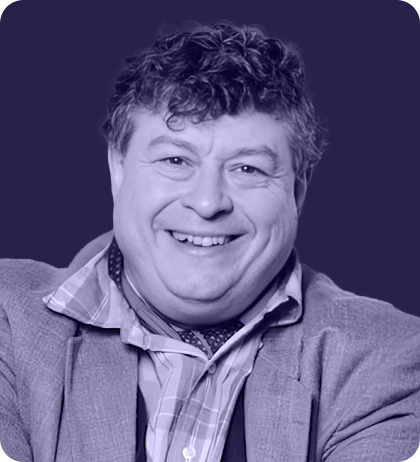 Smiling man with curly hair wearing a striped shirt, scarf, and textured jacket against a dark background.