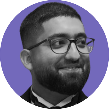 Smiling man with glasses, beard, and short hair, dressed in formal attire against a purple circular background.