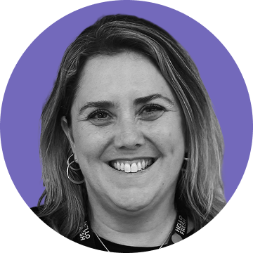 Smiling woman with shoulder-length hair, wearing hoop earrings and a lanyard, on a purple circular background.