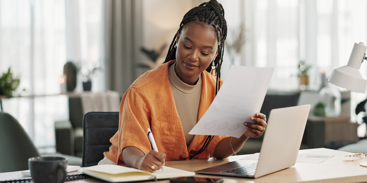 Professional woman reviewing documents and taking notes at a desk with a laptop, representing HOA board training and construction planning.