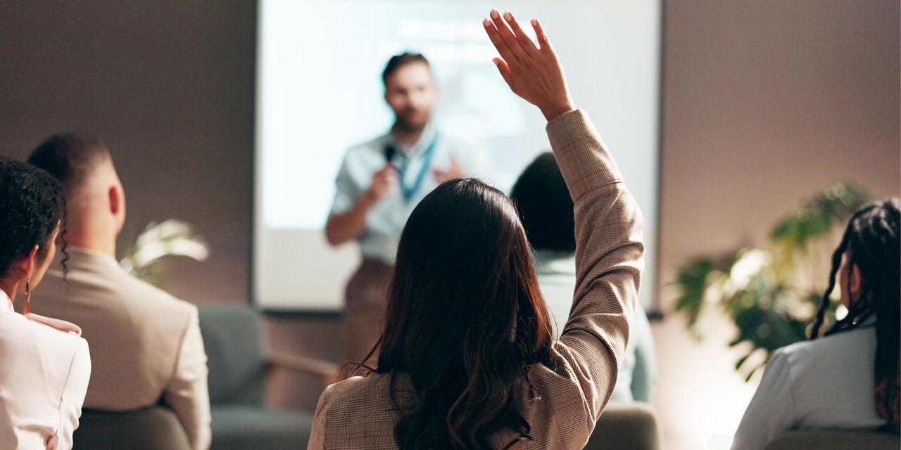Audience member raising a hand during a professional training seminar, representing an HOA board education webinar on association insurance.