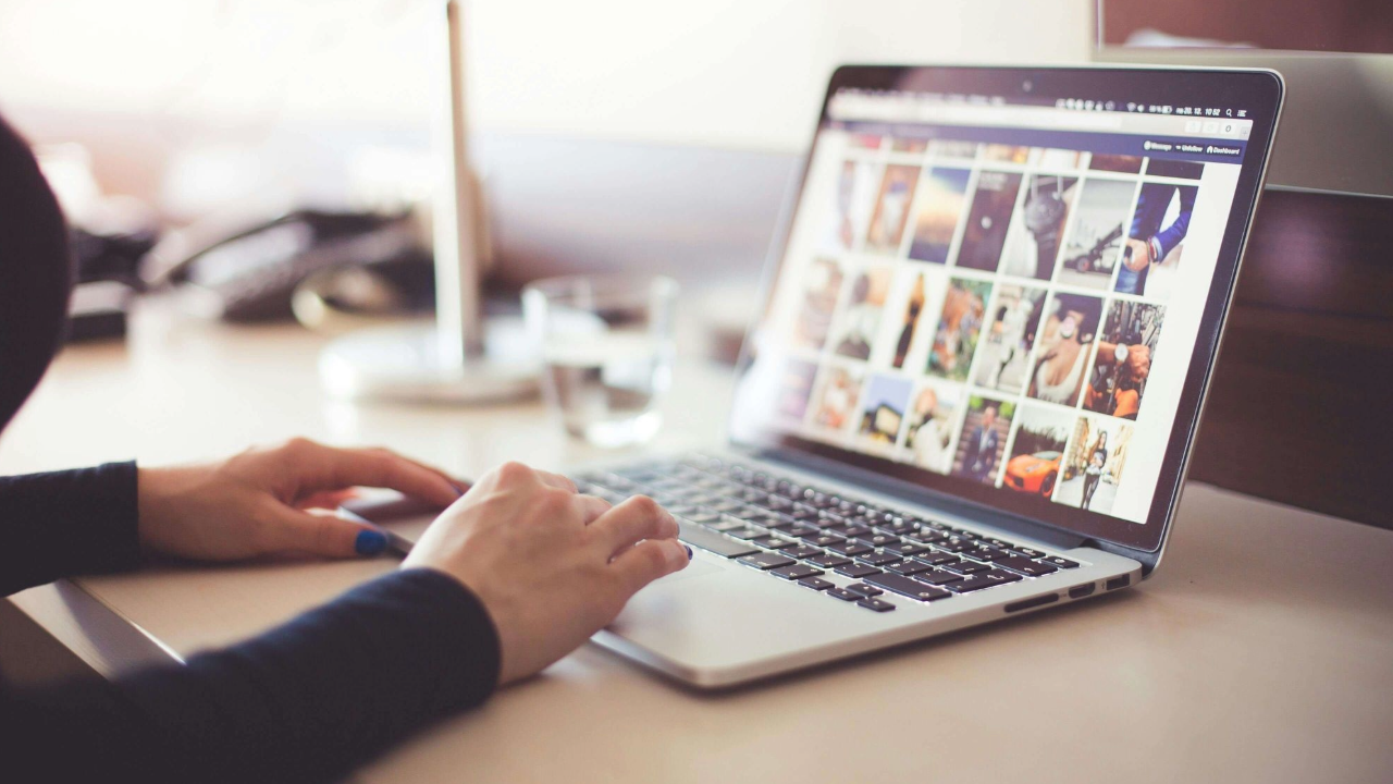 laptop on wooden desk showing photos on the screen, with hands on keyboard