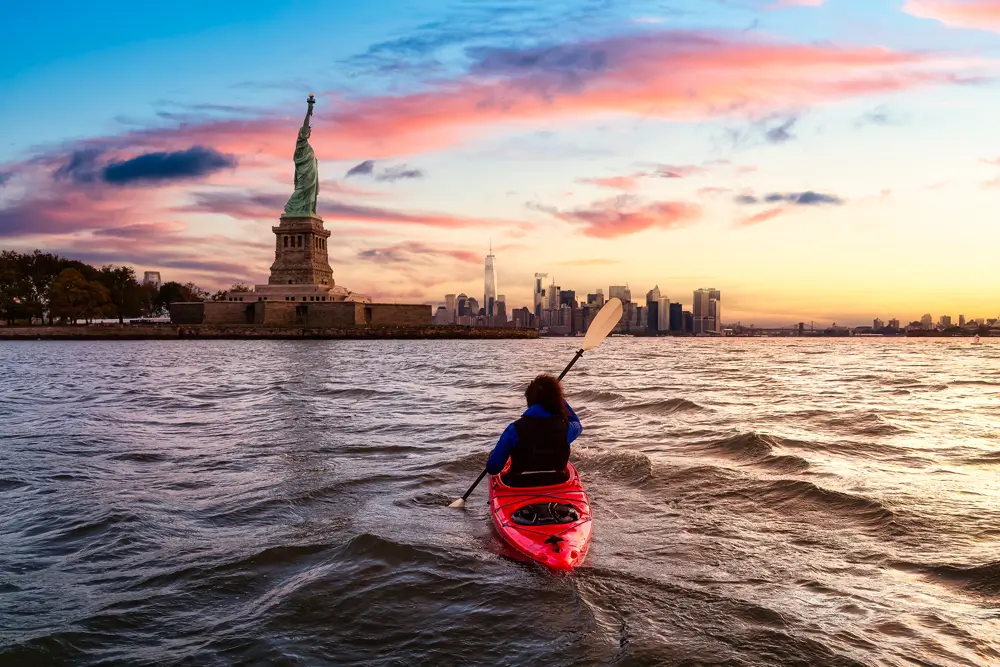 Kayaker on New York Harbor with the Statue of Liberty and Manhattan skyline at sunset