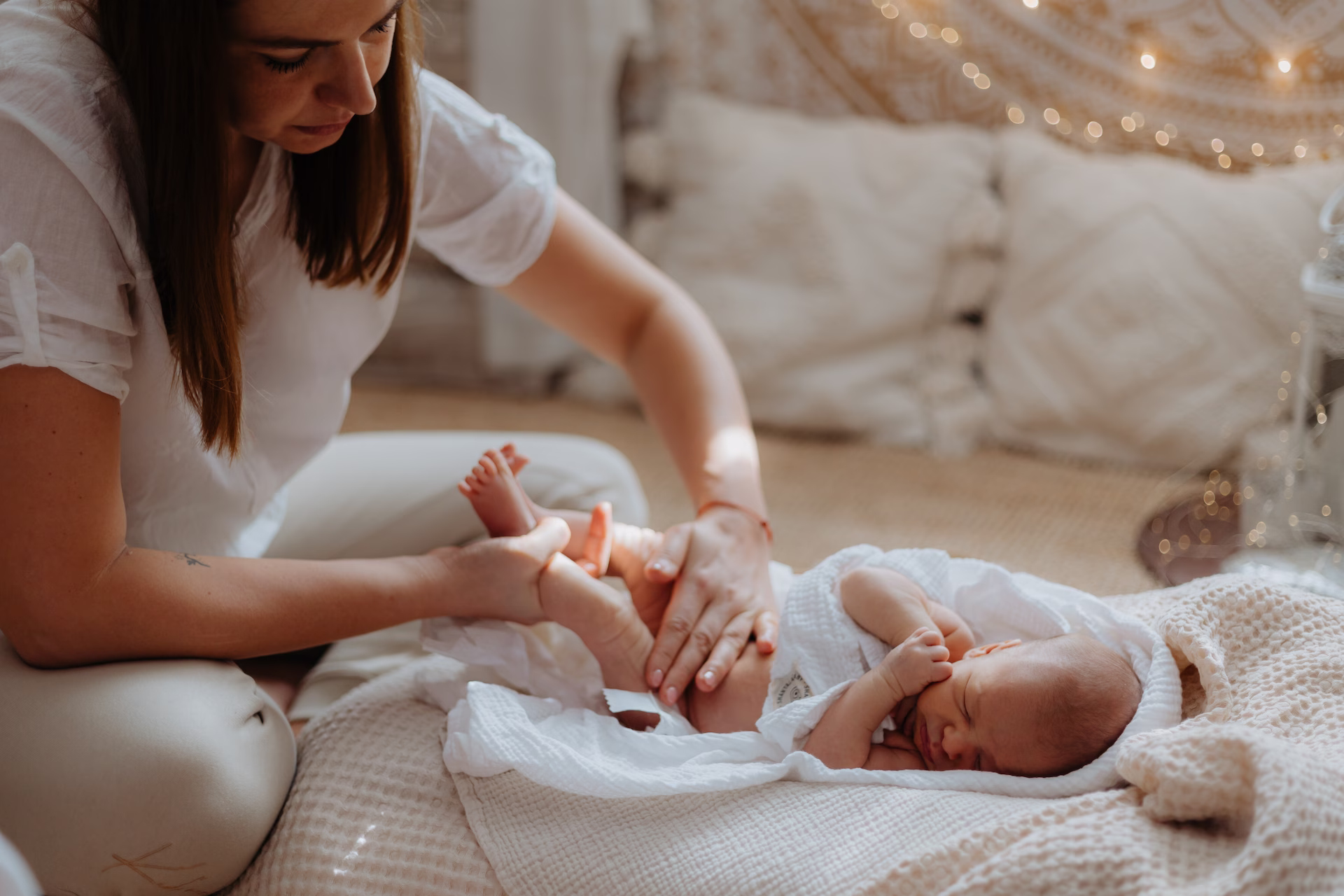 Woman gently changing or massaging diaper area of a newborn baby lying on a soft blanket indoors.