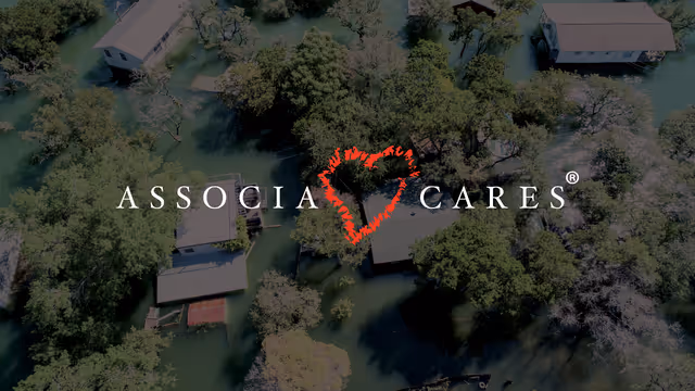 Aerial view of flooded residential area surrounded by trees, with the "ASSOCIA CARES" logo and a red heart symbol overlaid at the center. Ask ChatGPT