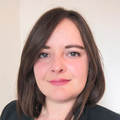 Close-up portrait of a woman with shoulder-length brown hair, light skin, and a slight smile wearing a dark blazer.