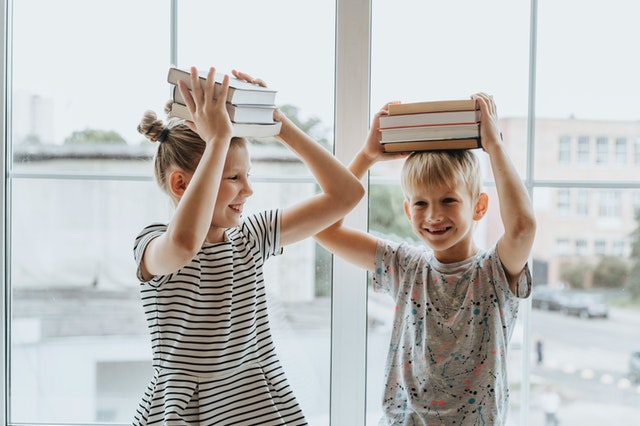 Two young kids balancing books on their head