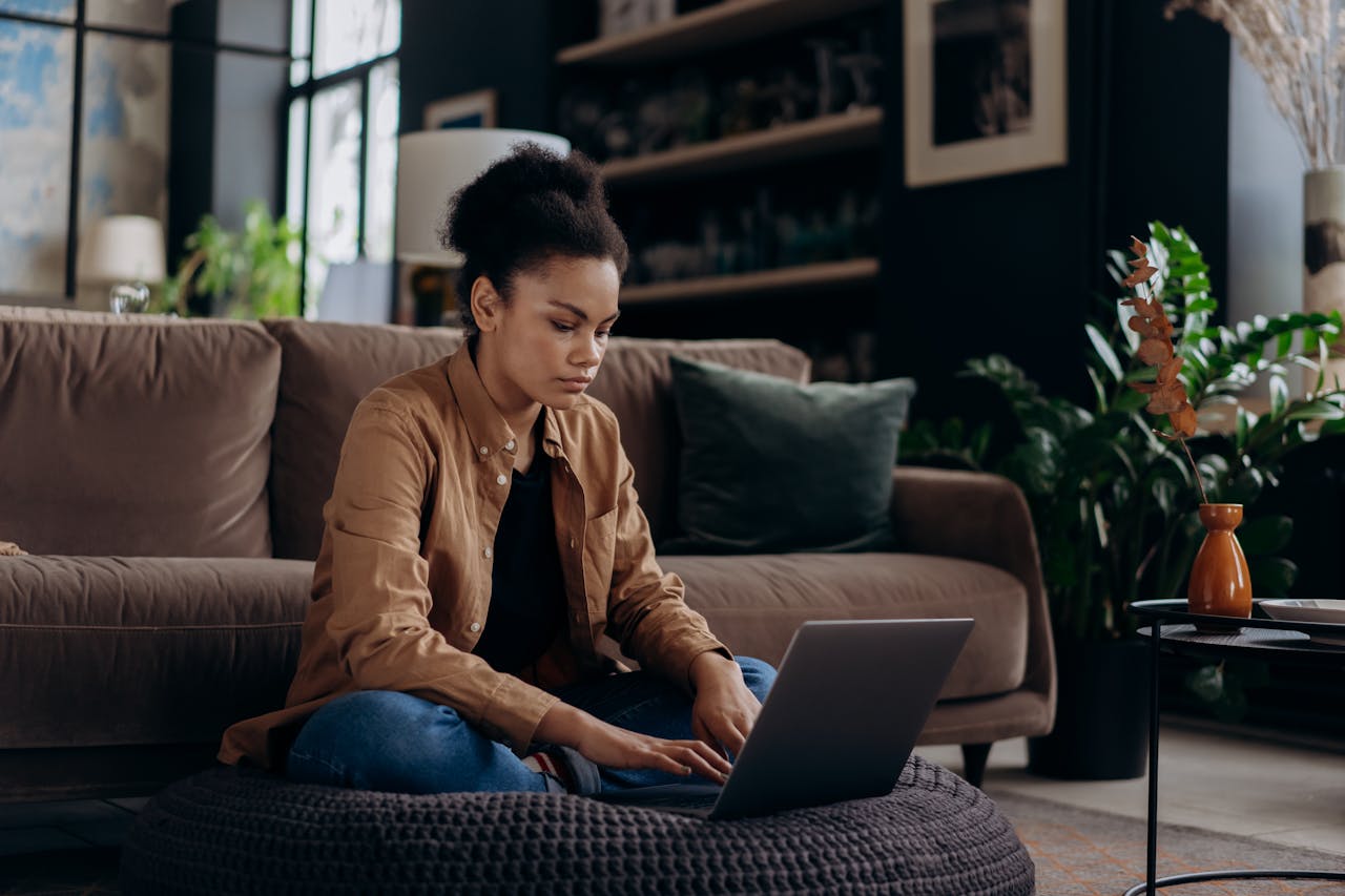 Woman Sitting on Black Knitted Floor Cushion while Using Laptop