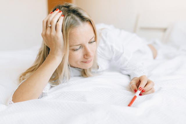 A Woman Looking at a Pregnancy Test while Lying in Bed
