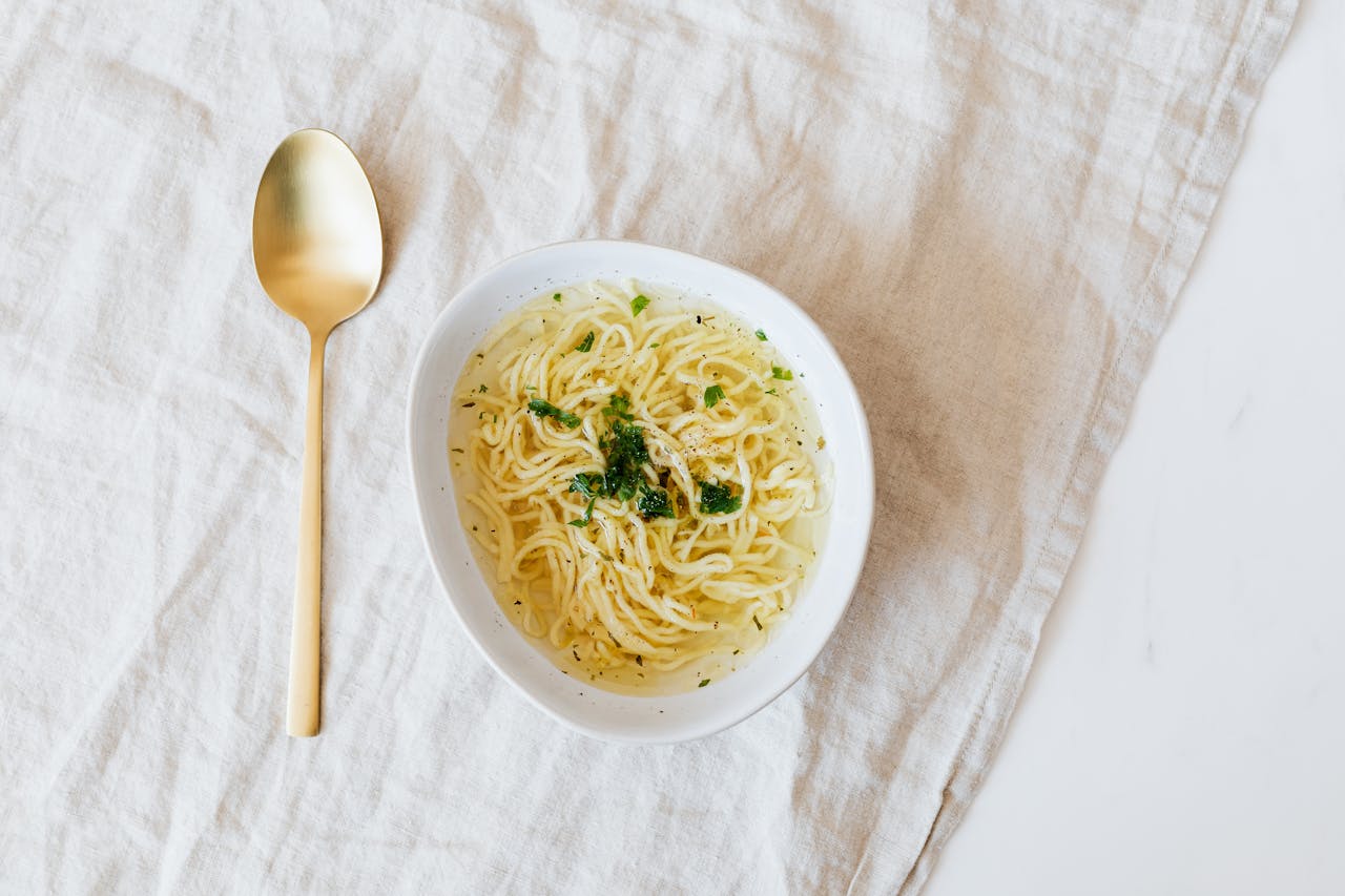 Bowl of noodles with gold plated spoon on table