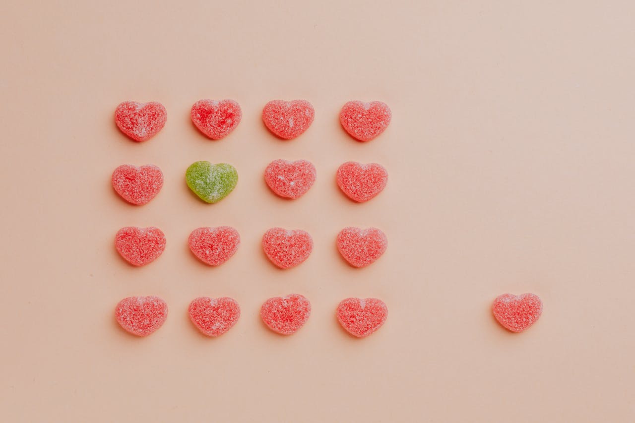 Heart shaped gummy candy assorted in rows with one candy aside against pink background