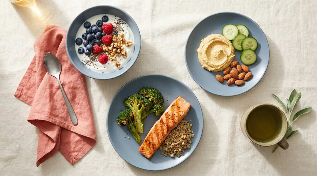 Overhead view of a PCOS-friendly meal spread — Greek yogurt parfait, grilled salmon with broccoli and quinoa, hummus with vegetables