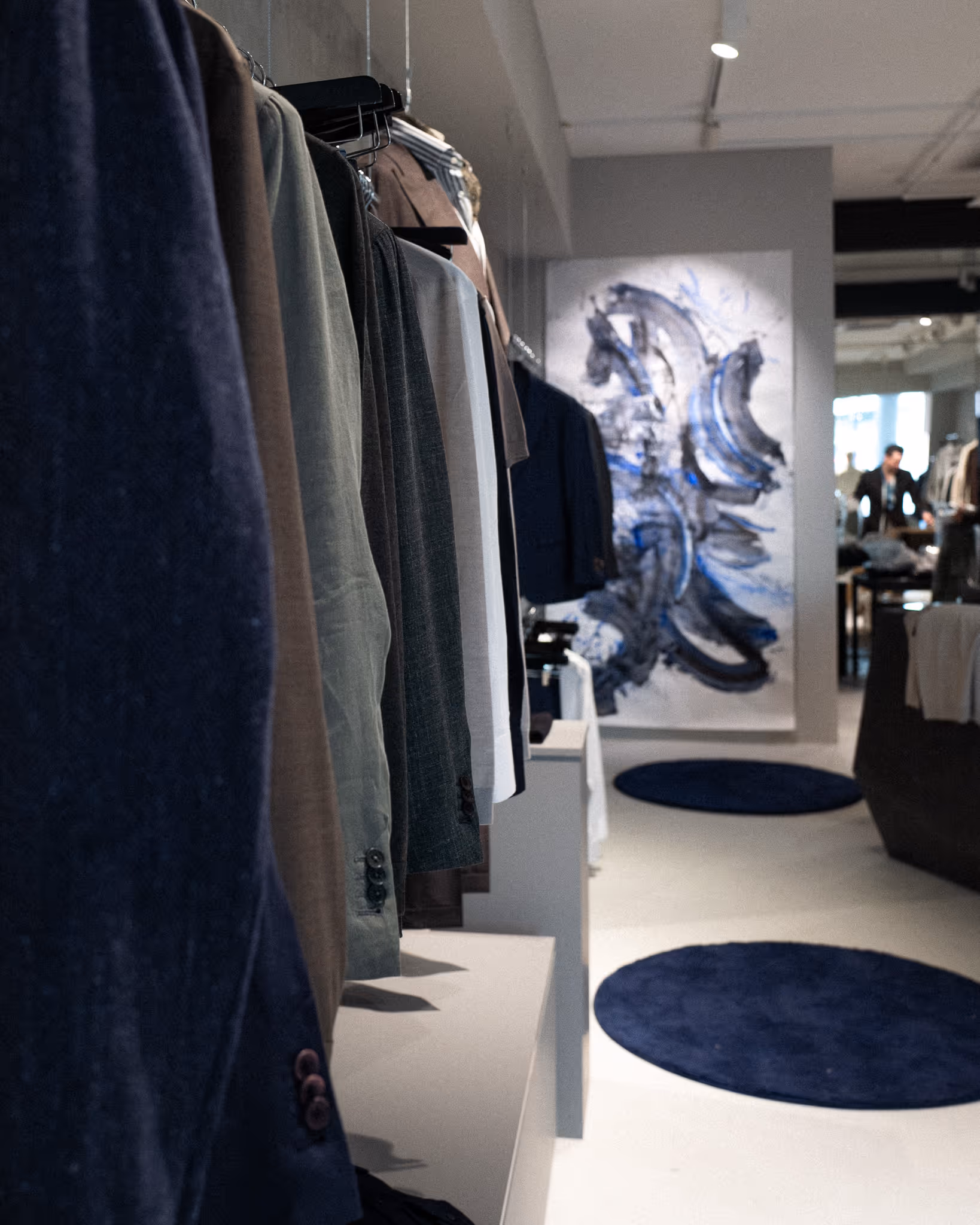 Blick in den HOUSE OF MERCURY Store in Dortmund mit hängenden Maßanzügen und moderner Kunst an der Wand – hochwertige Herrenmode im modernen Interior.