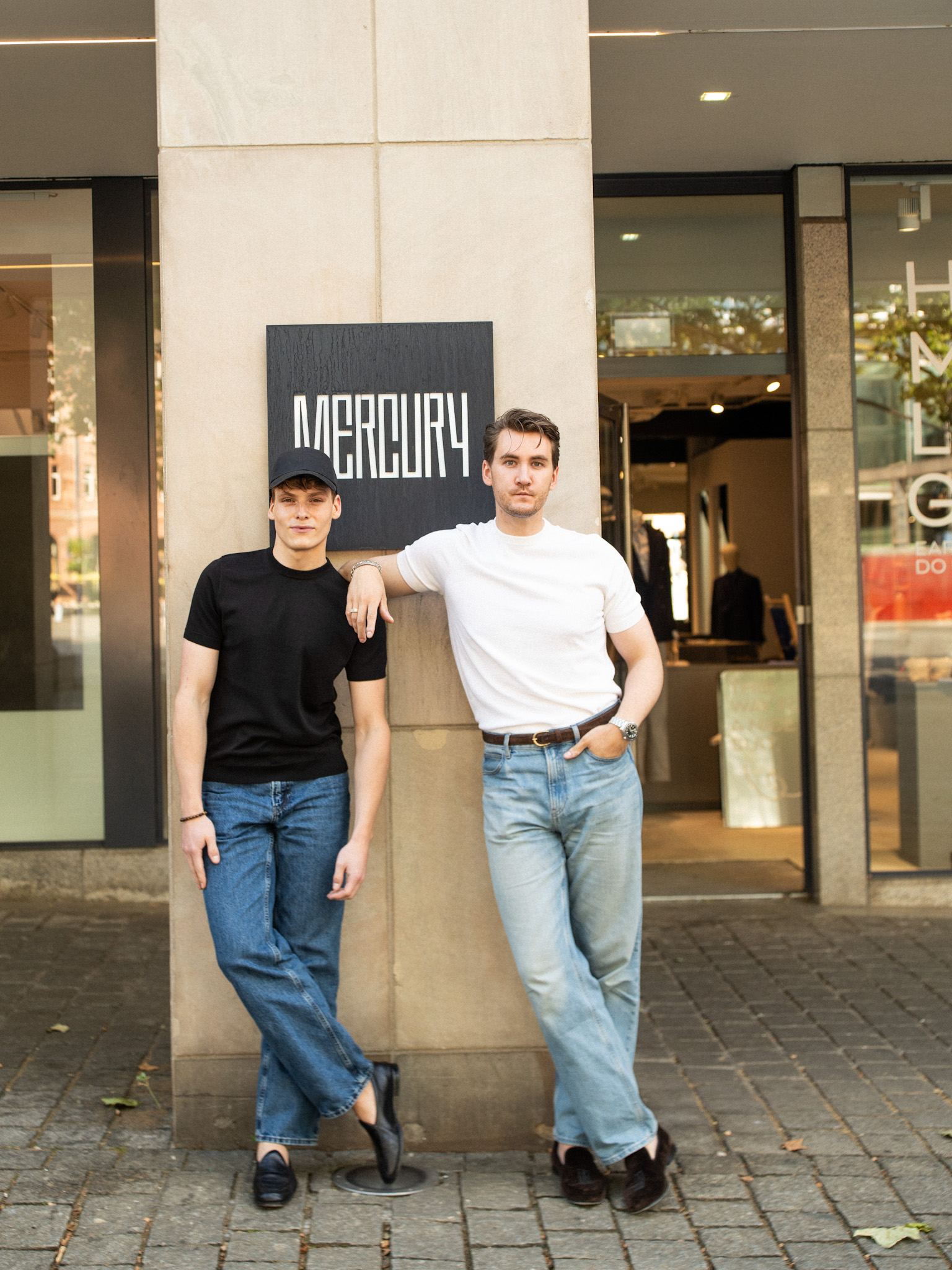 Two men standing in front of the HOUSE of MERCURY Flagship Store in Dortmund. Both are wearing a jeans and loafers, paired with a cotton silk knit shirt.