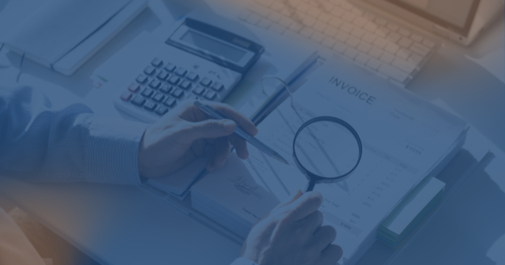 mesa com documentos e mão segurando uma lupa