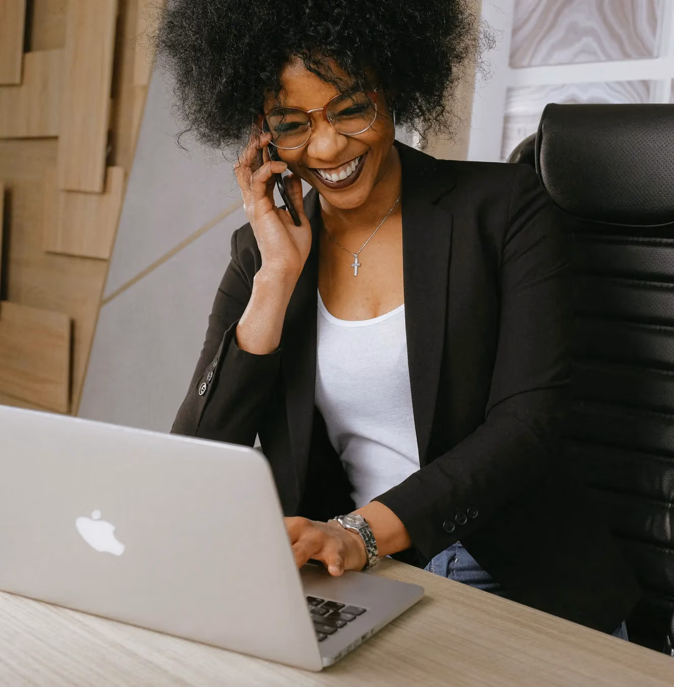 Femme souriante parlant au téléphone tout en travaillant sur un ordinateur portable dans un bureau.