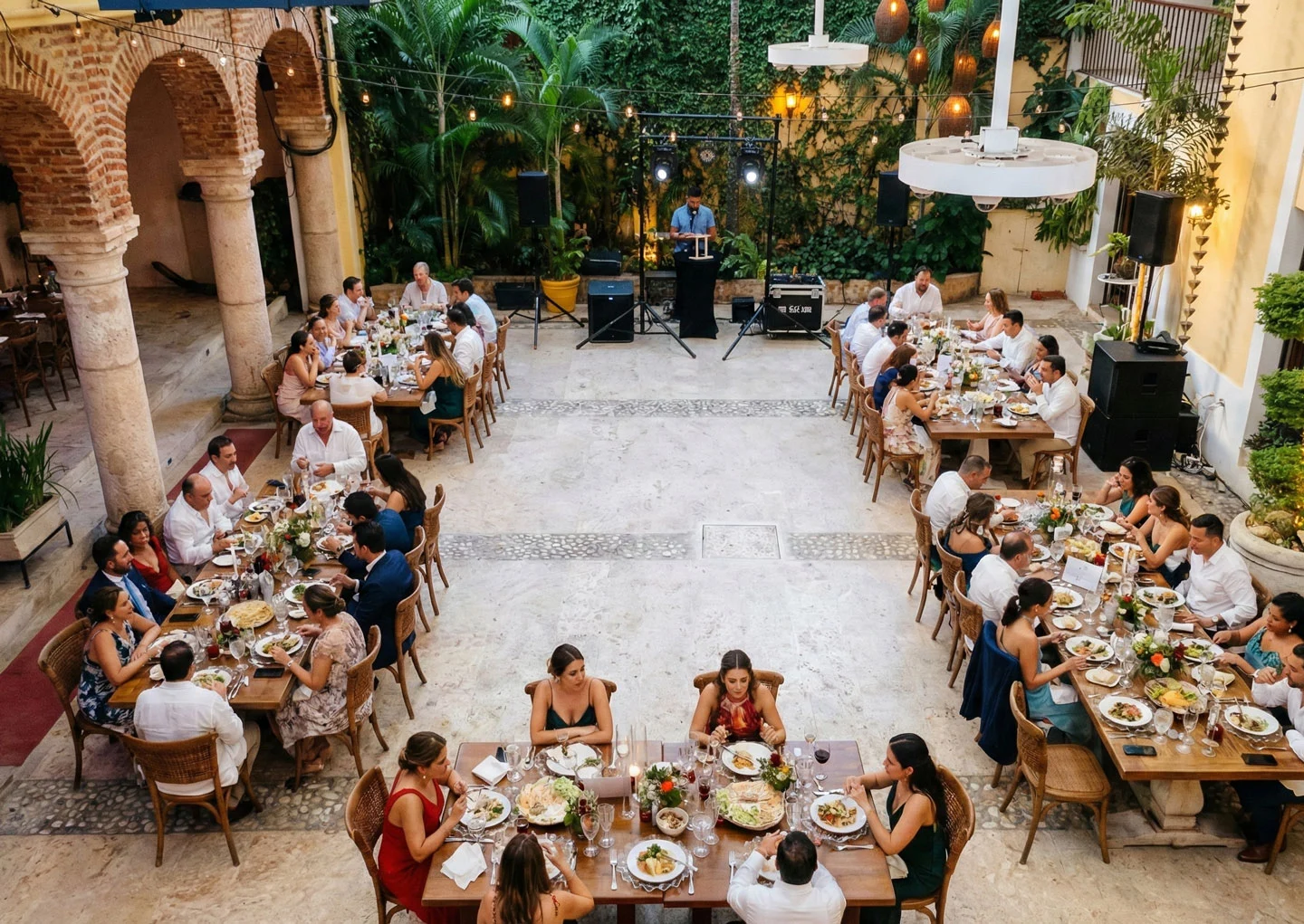 Outdoor banquet with multiple tables where guests are seated eating and a speaker on a podium in front of a green ivy wall.
