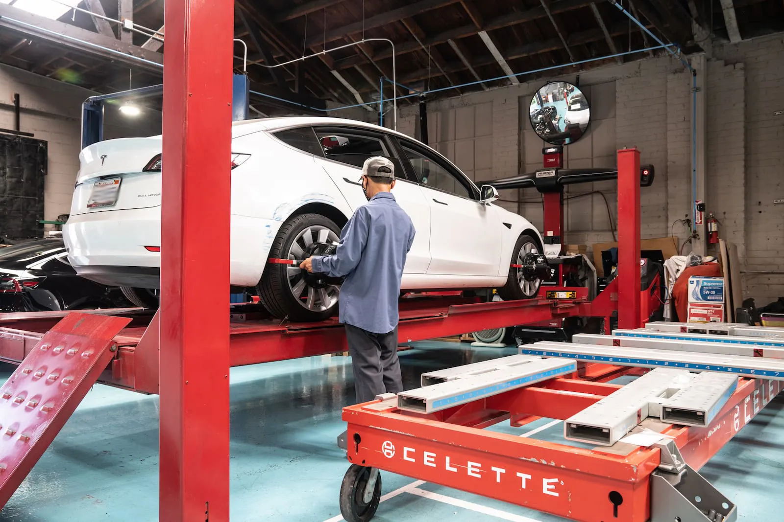 Mechanic using wheel alignment equipment on a white Tesla car lifted in a garage.