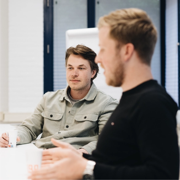 Supply Chain & Operations professional zit met zijn leidinggevende aan tafel en vertelt een verhaal met handgebaren erbij. 