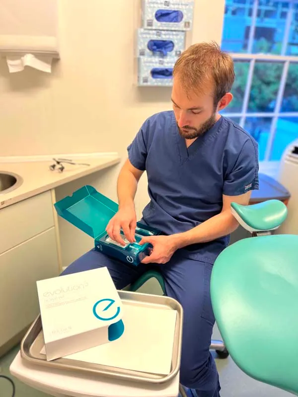 Male dental professional in navy scrubs opening a teal sterilization pouch in a dental clinic.