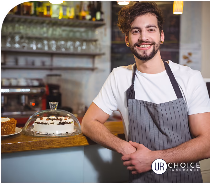 Smiling young male barista wearing apron standing behind counter with cakes in a cafe.