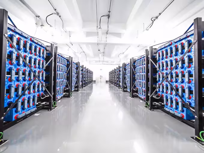Large room filled with rows of blue and black battery racks, illuminated by overhead lights.
