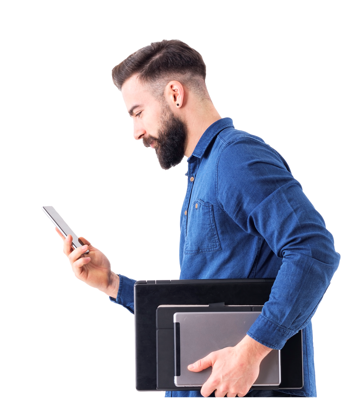 Bearded man in blue shirt holding laptop, tablet and looking at smartphone in his hand.