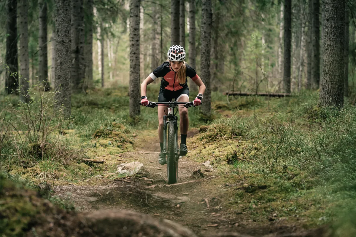 Kvinna i skogen på MTB-cykel med hjälm.
