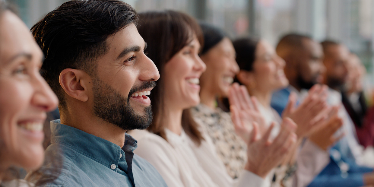 Audience of diverse professionals smiling and applauding during a corporate event or announcement