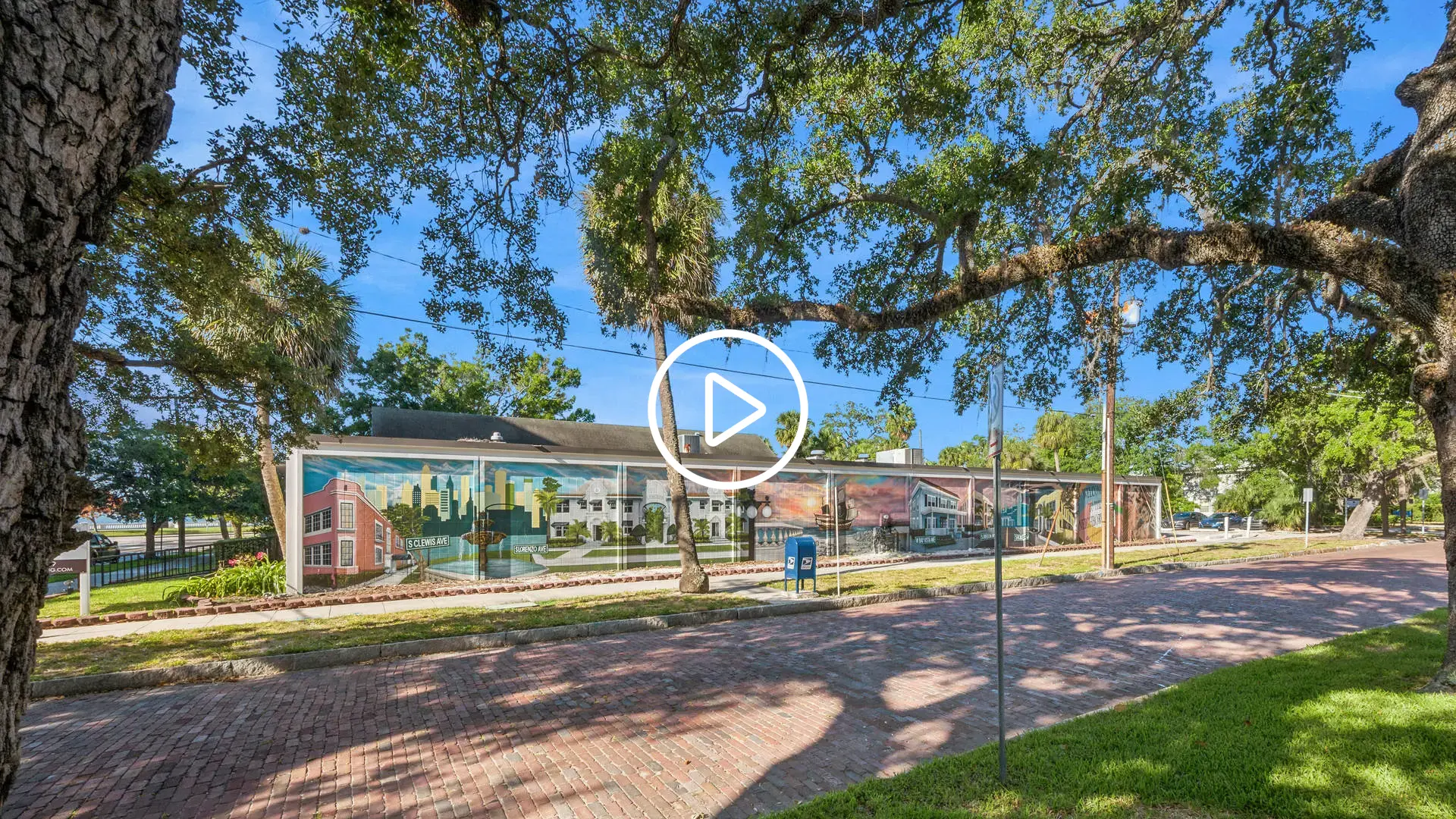 Video cover image showing a mural-covered building on a tree-lined brick street.