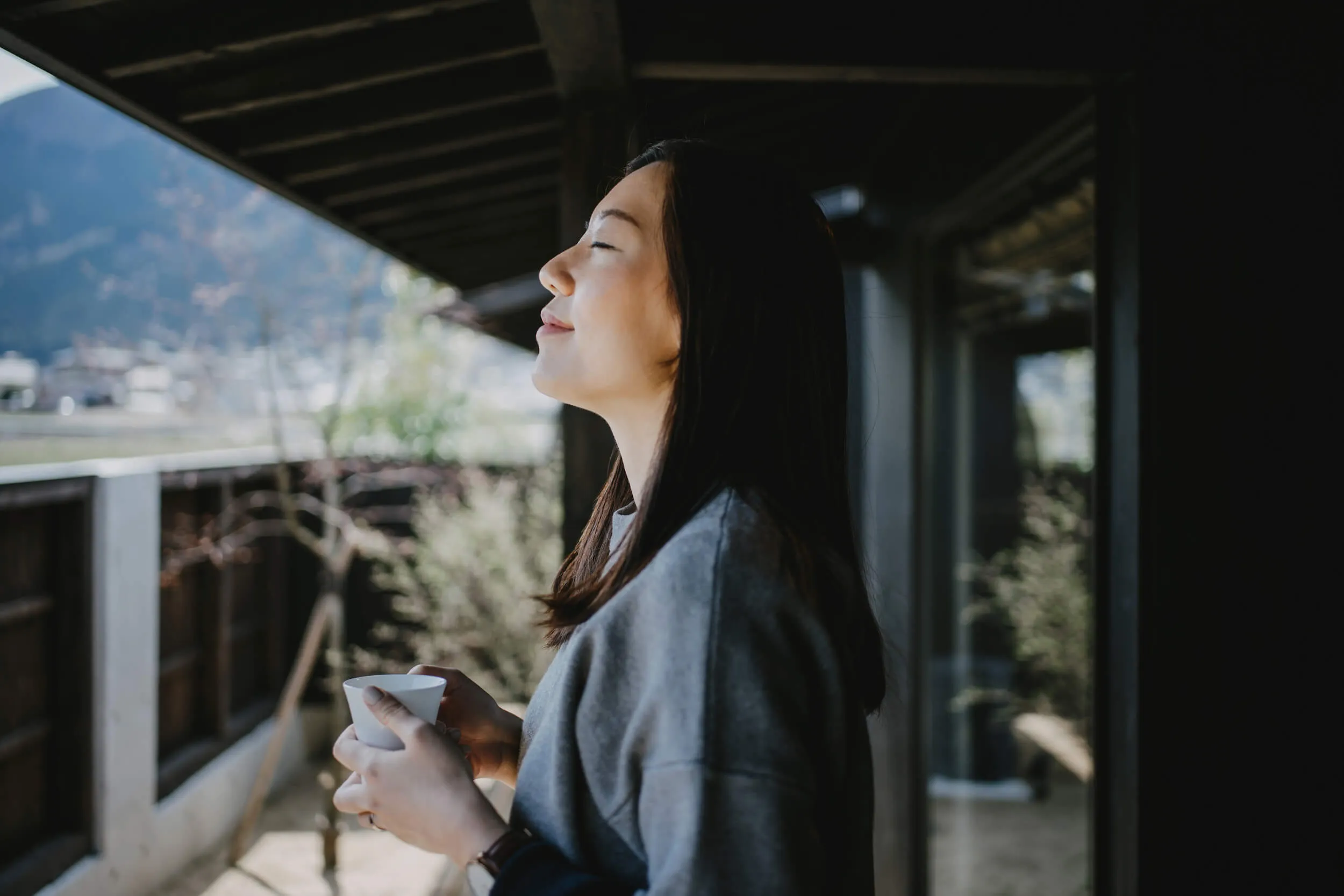 Young woman breathes fresh air from a balcony with a coffee cup in her hand