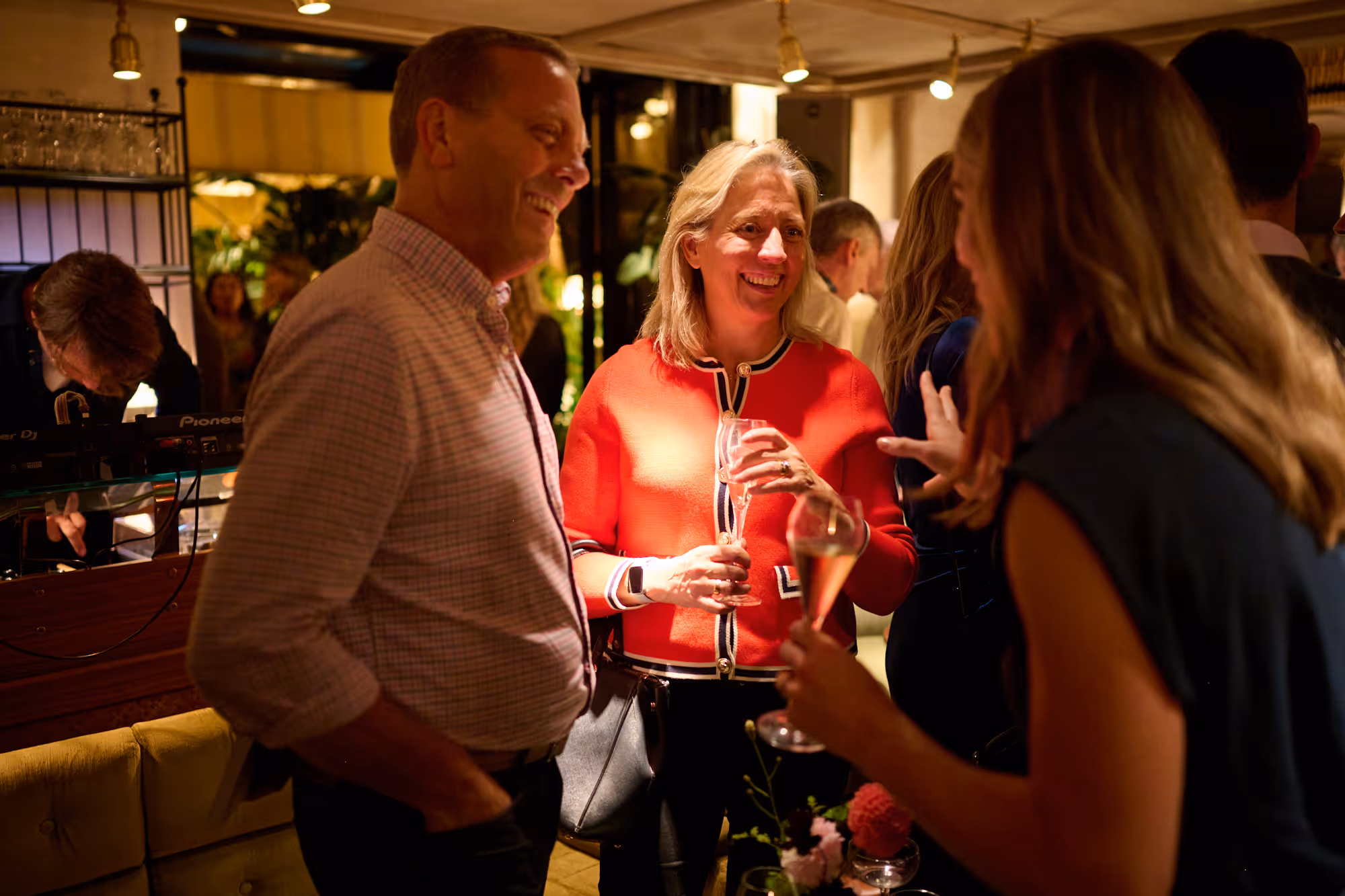 Couple laughing and smiling in conversation with another in elegant bar with greenery in the distance